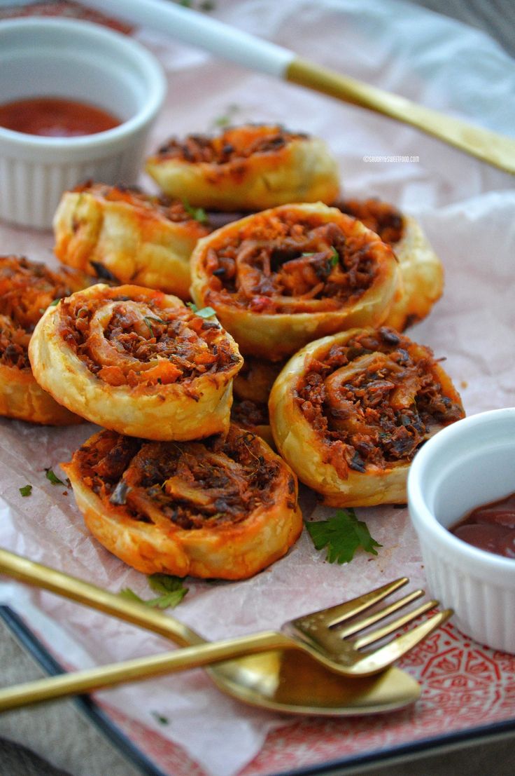 some tasty looking pastries are on a plate with sauce and gold spoons