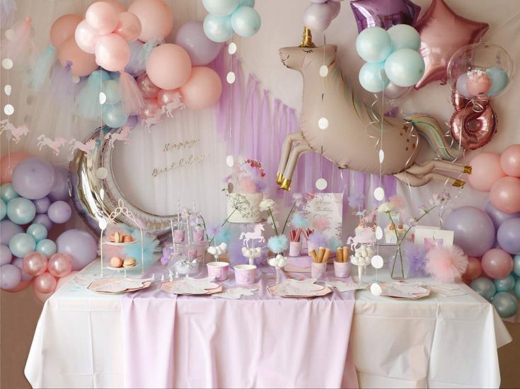 a table topped with lots of balloons next to a unicorn cake and cupcakes