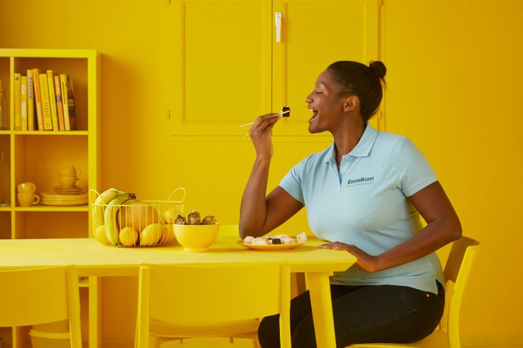 a woman sitting at a yellow table with food in front of her and she is eating