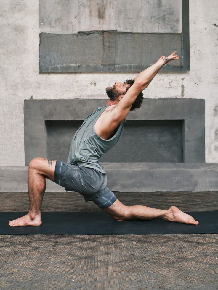 a man is doing yoga outside in front of a concrete wall and fireplace with his legs spread out