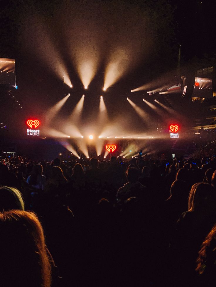 a large group of people at a concert with their lights on and the stage lit up