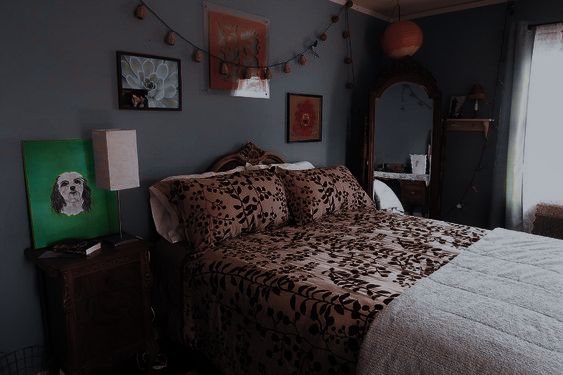 a bed sitting in a bedroom next to a window with curtains and pictures on the wall