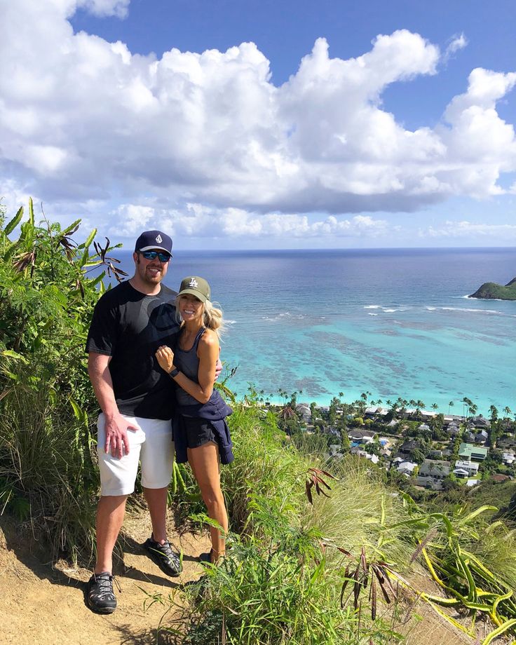 a man and woman standing on top of a hill next to the ocean with palm trees