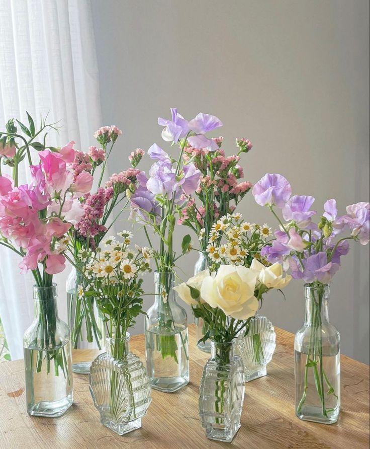 several vases filled with different types of flowers on a wooden table next to a window