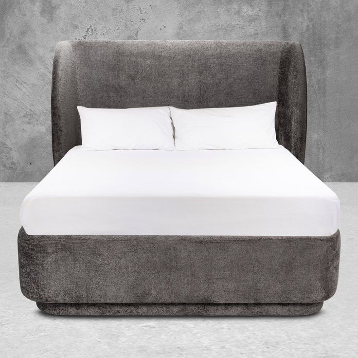 an upholstered bed with white sheets and pillows is shown in front of a concrete wall