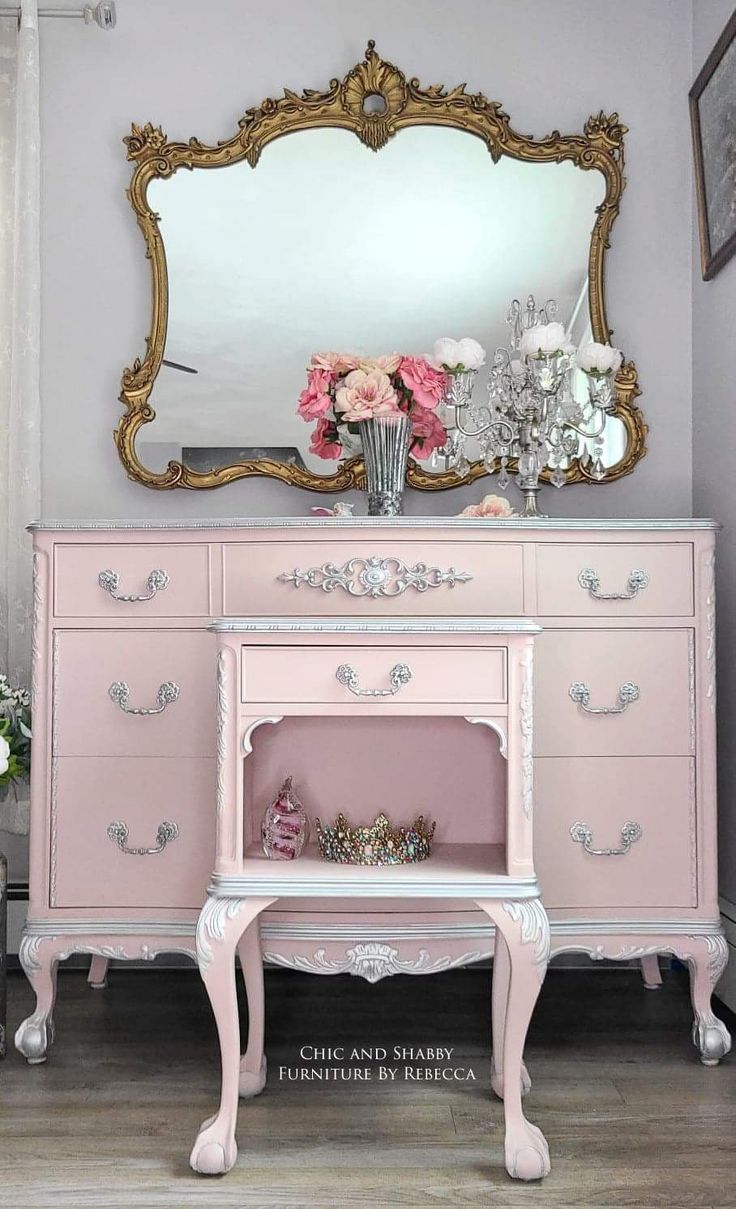 a pink dresser with flowers on top and a large mirror above it in a room