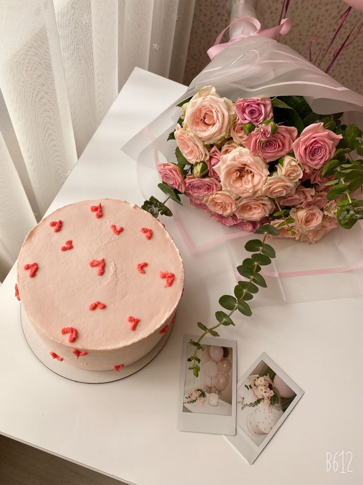 a white table with a pink cake and bouquet of flowers on it next to a window