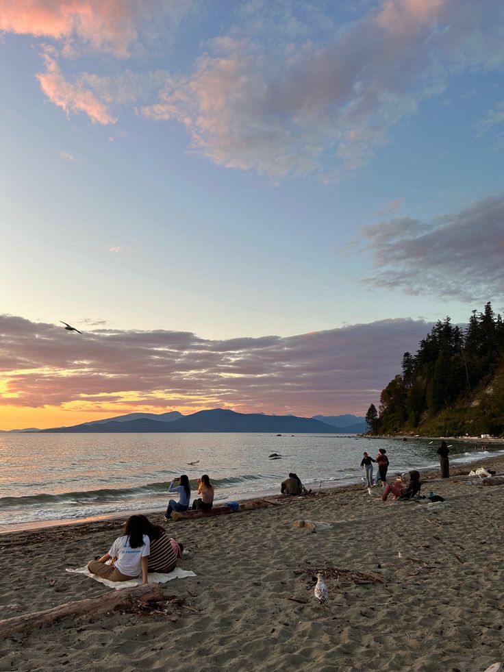 people are sitting on the beach at sunset