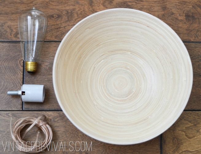 a white bowl sitting on top of a wooden floor next to an electric light bulb