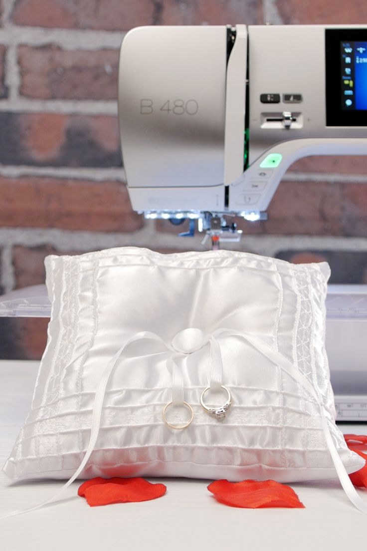 two wedding rings are placed on a pillow next to a sewing machine and red petals