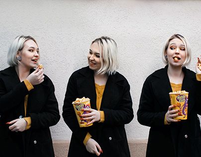 three women standing in front of a wall eating food