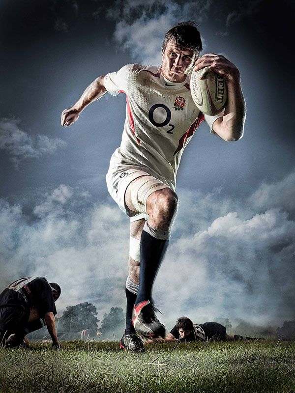 a rugby player is running with the ball in his hand and two other players are on the ground behind him