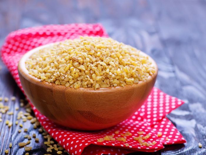 a wooden bowl filled with sesame seeds on top of a red and white checkered cloth