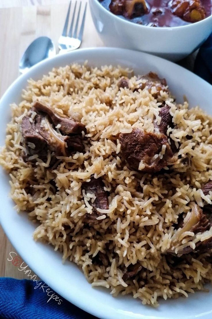 a white plate topped with rice and meat next to a bowl of sauce on a table