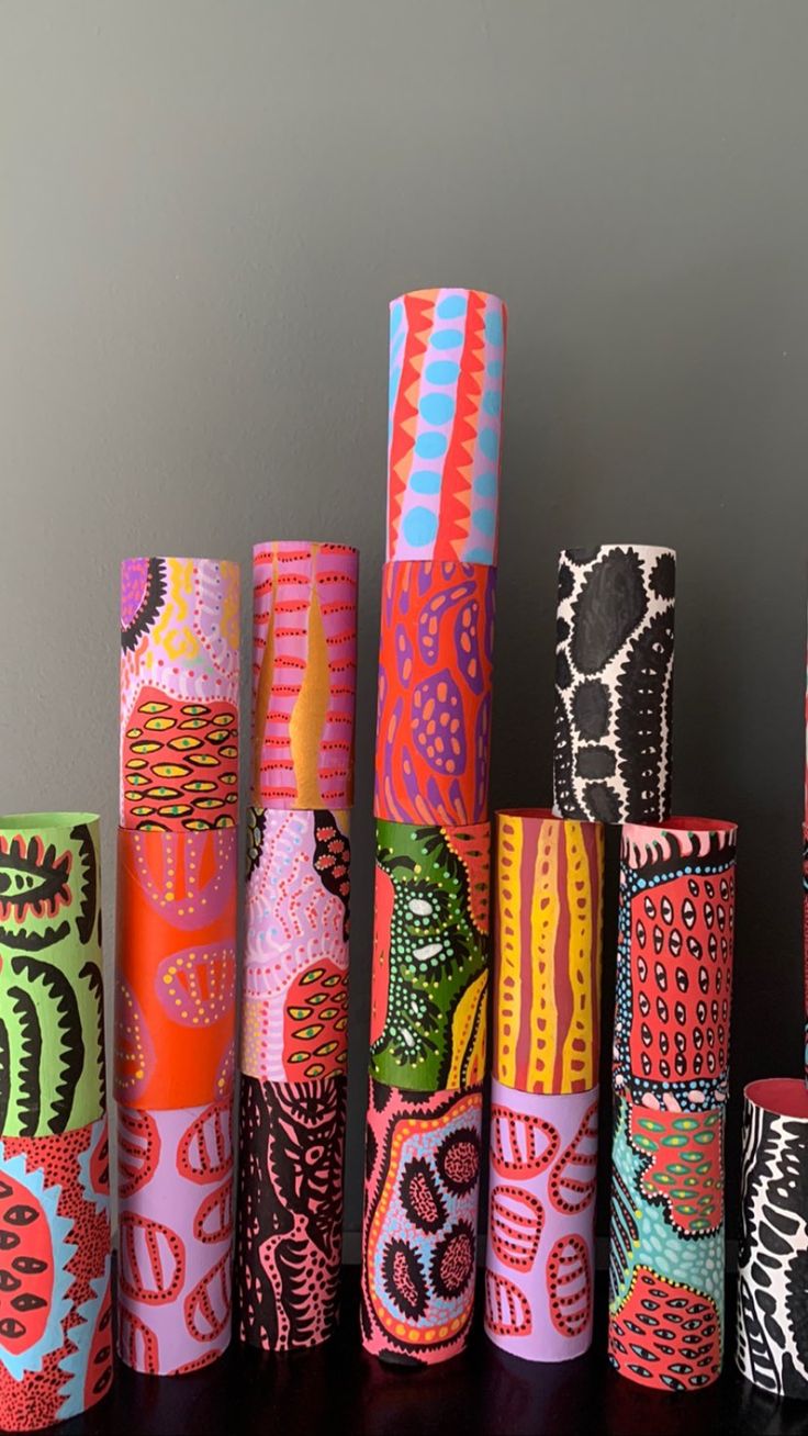 many different colored paper rolls are lined up on a table with gray wall in the background