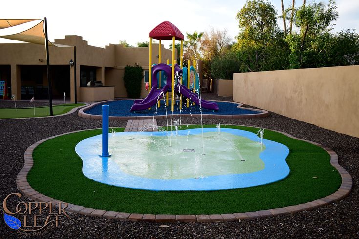 a water play area in the middle of a courtyard with artificial grass and colorful slides