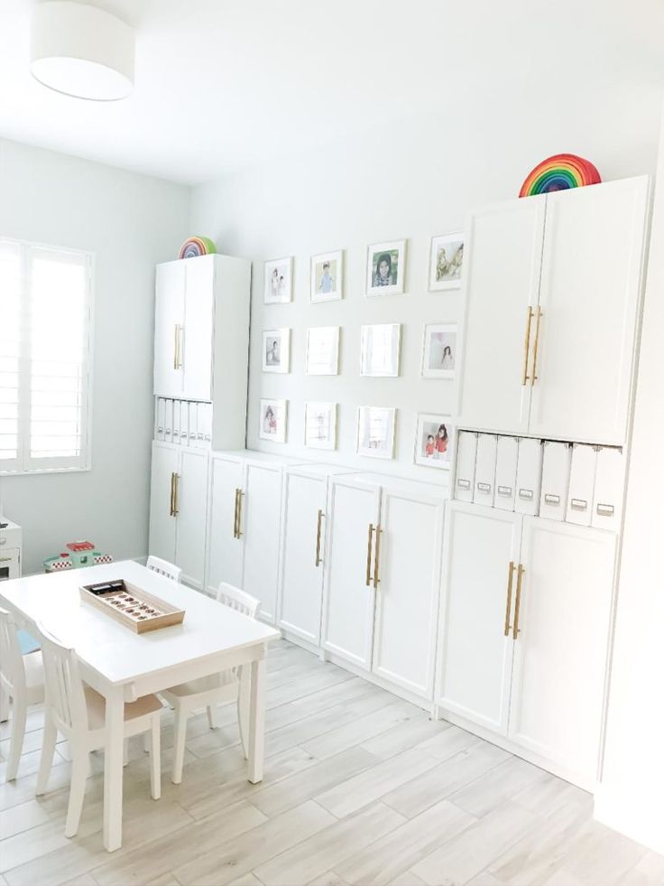 a white kitchen with lots of cabinets and drawers on the wall, along with a dining table