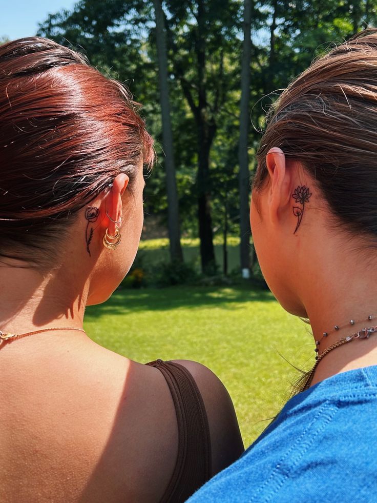 two women with tattoos on their backs looking at each other in front of some trees