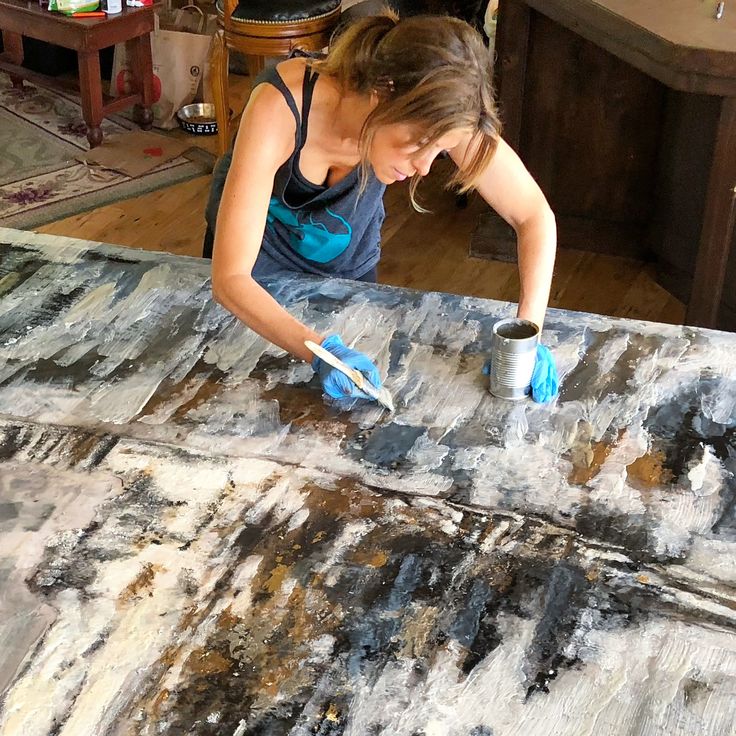 a woman in blue gloves painting on an old piece of wood with black and white paint