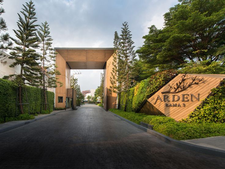 the entrance to an apartment complex with trees and bushes on either side of the road