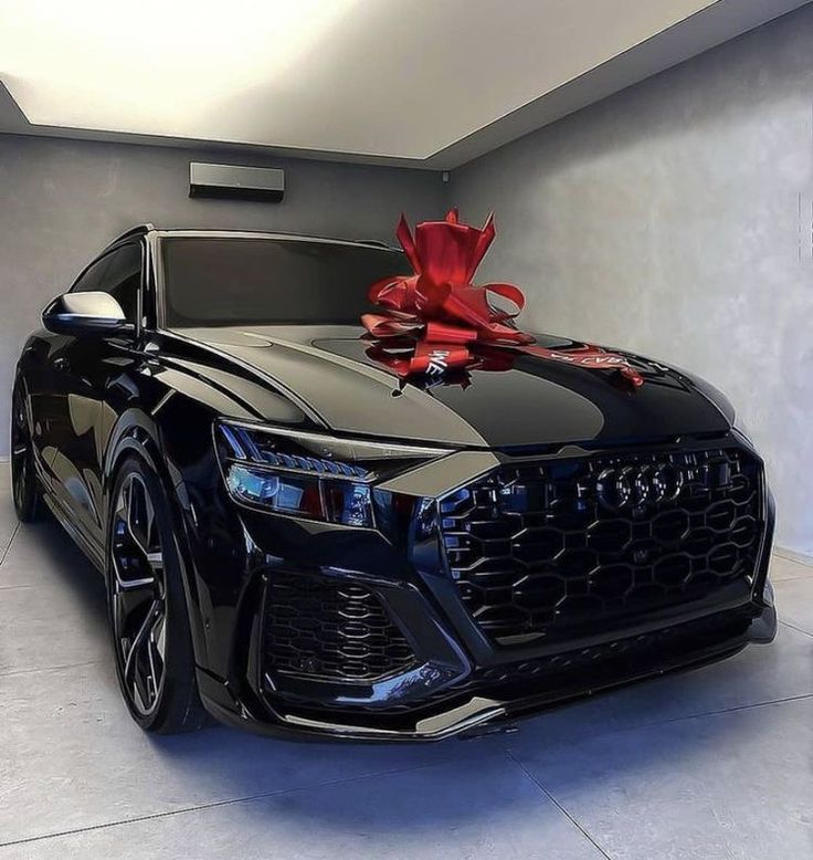 a black car with a red bow on the hood is parked in a garage next to a wall