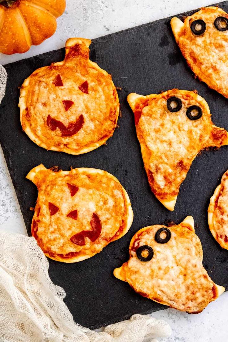 mini halloween pizzas with faces and eyes are on a baking sheet next to pumpkins