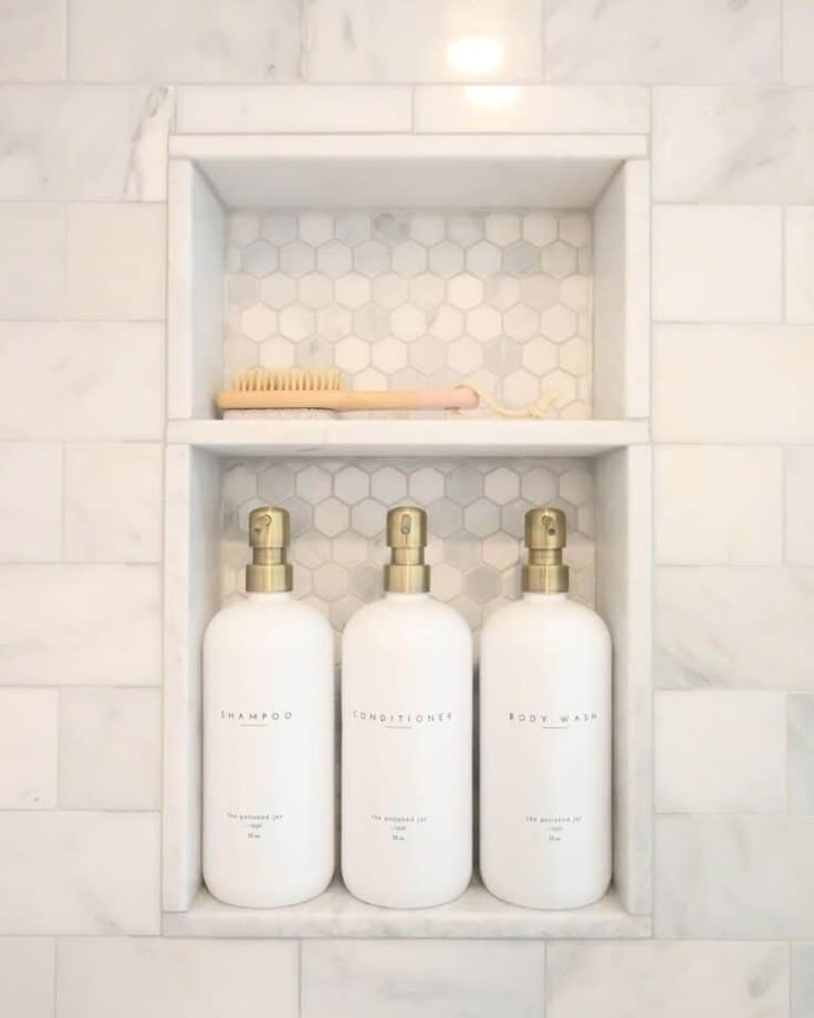 three white bottles with gold handles in a shelf above a marble tiled wall and floor