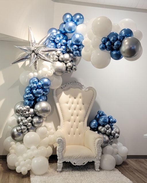 a balloon arch with blue and white balloons on it, an old chair in the middle