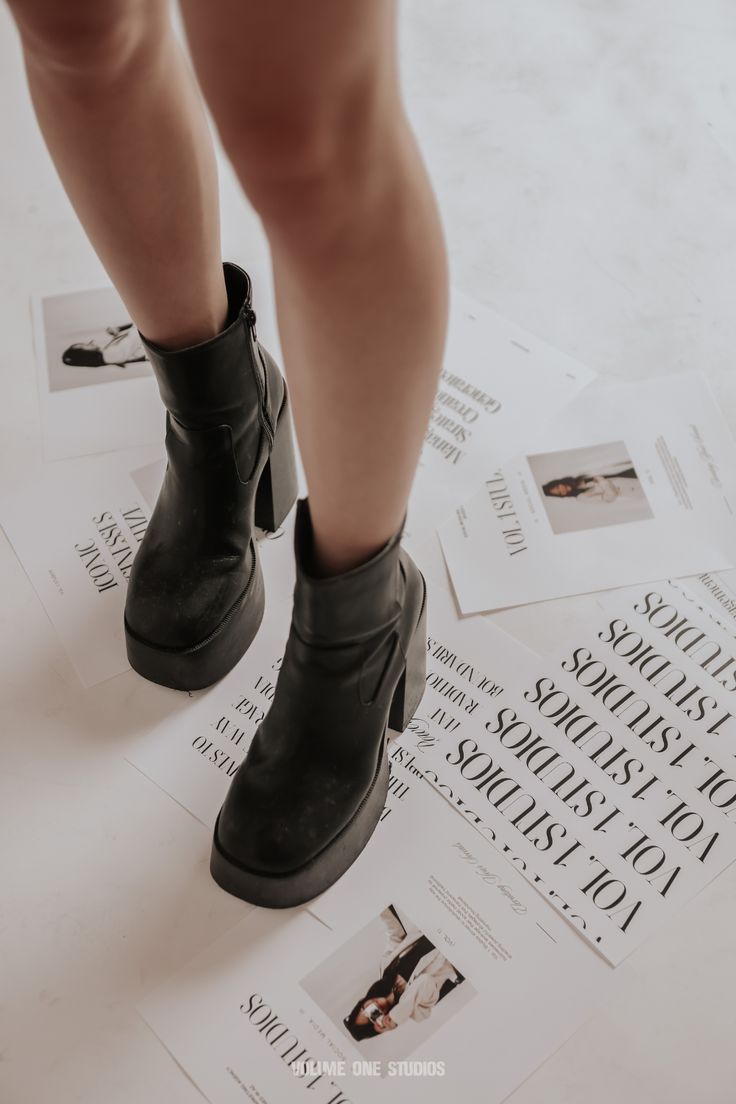 a woman's legs and black boots on top of newspaper