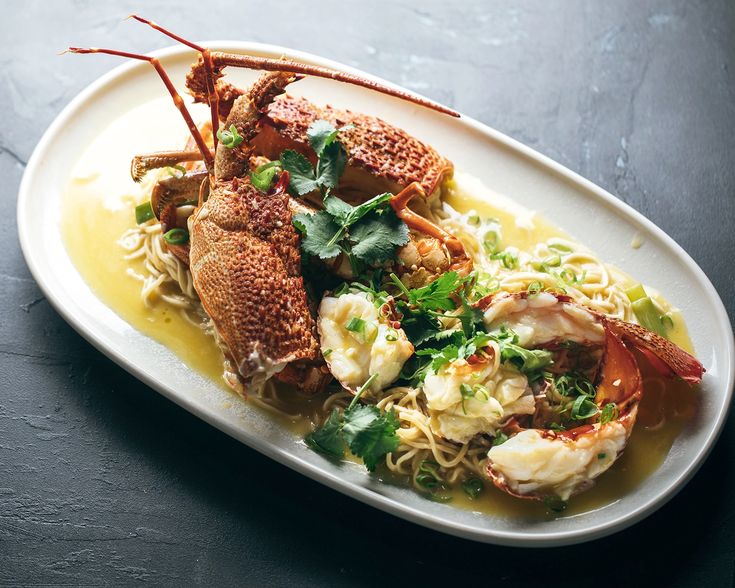 a white plate topped with pasta and lobster on top of a black table next to a fork