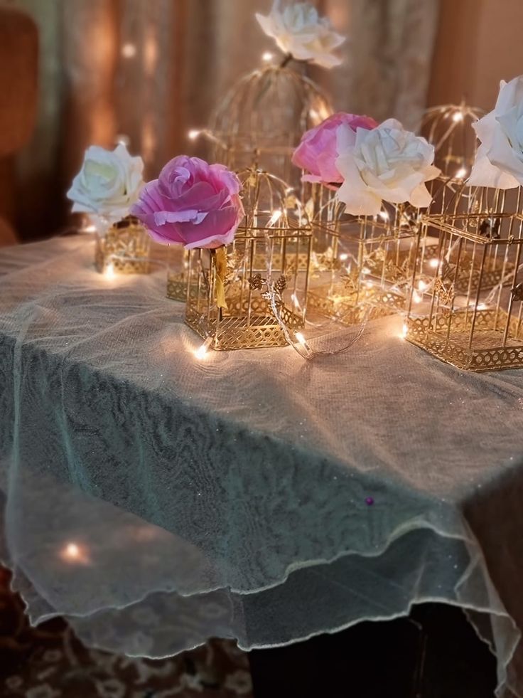 some pink and white flowers are in small cages on a table with lights around them