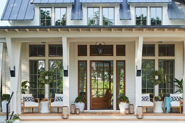 the front porch of a white house with potted plants and chairs on the steps