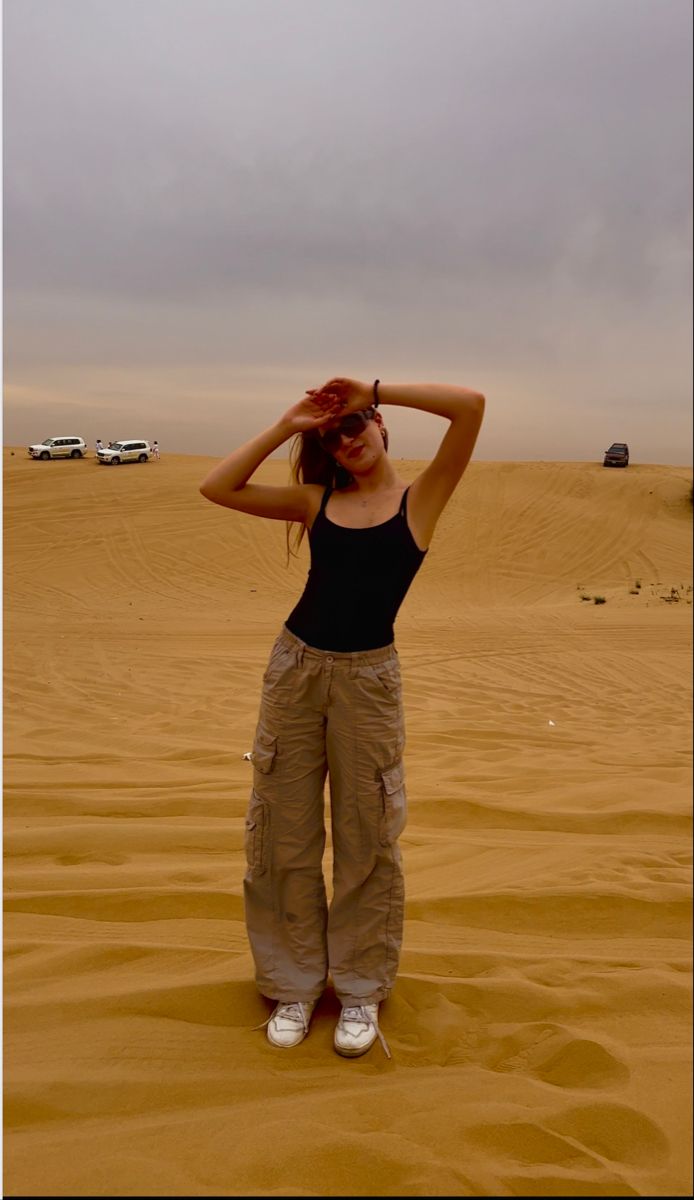 a woman is standing in the desert with her hands on her head and wearing cargo pants