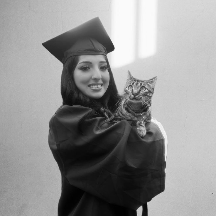 a woman holding a cat in her arms while wearing a graduation cap and gown on