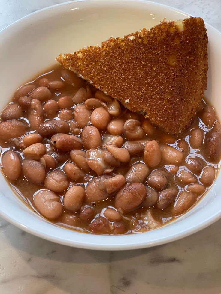 a white bowl filled with beans next to a piece of bread