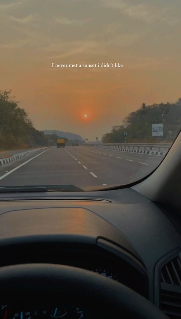 the sun is setting over a highway with cars driving on it and trees in the distance