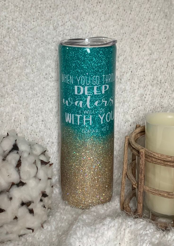 a candle next to a blue and gold glittered tumbler on a white blanket