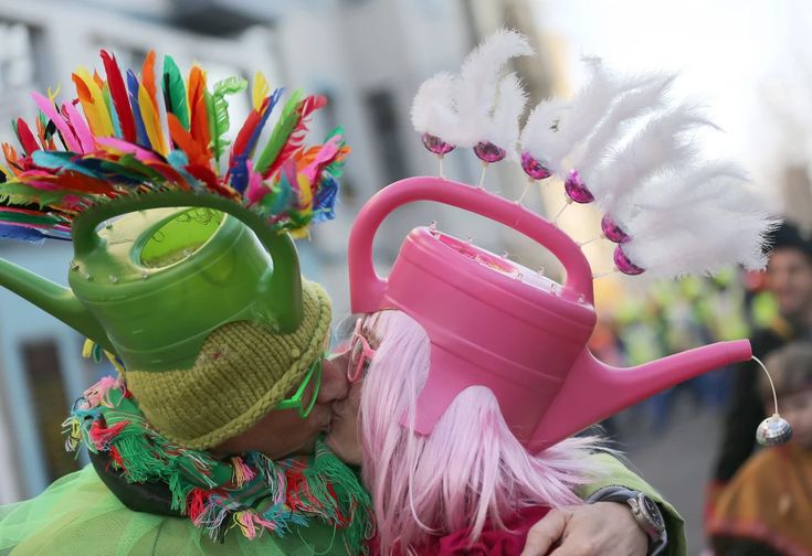 two people dressed in costumes with hats and watering cans on their heads, one is kissing the other