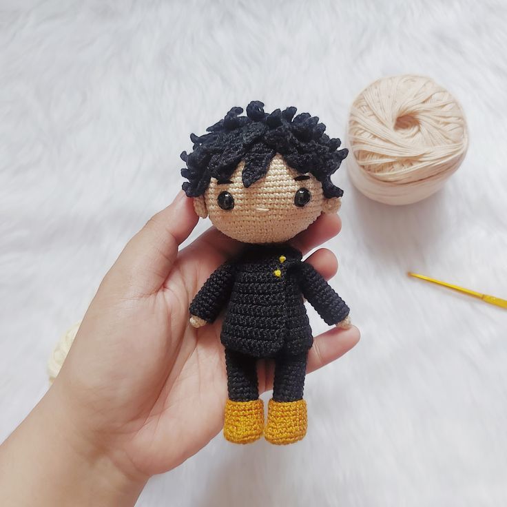 a hand holding a tiny doll next to a ball of yarn