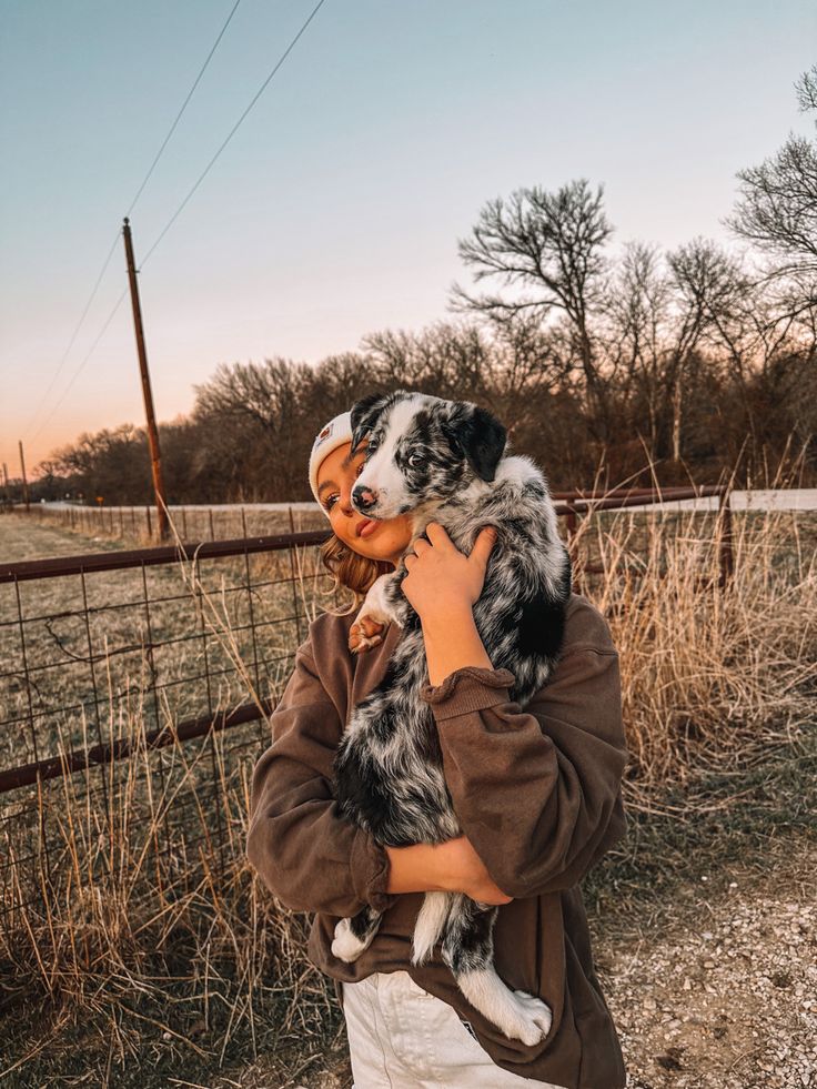 a woman holding a dog in her arms while standing next to a fence and grass