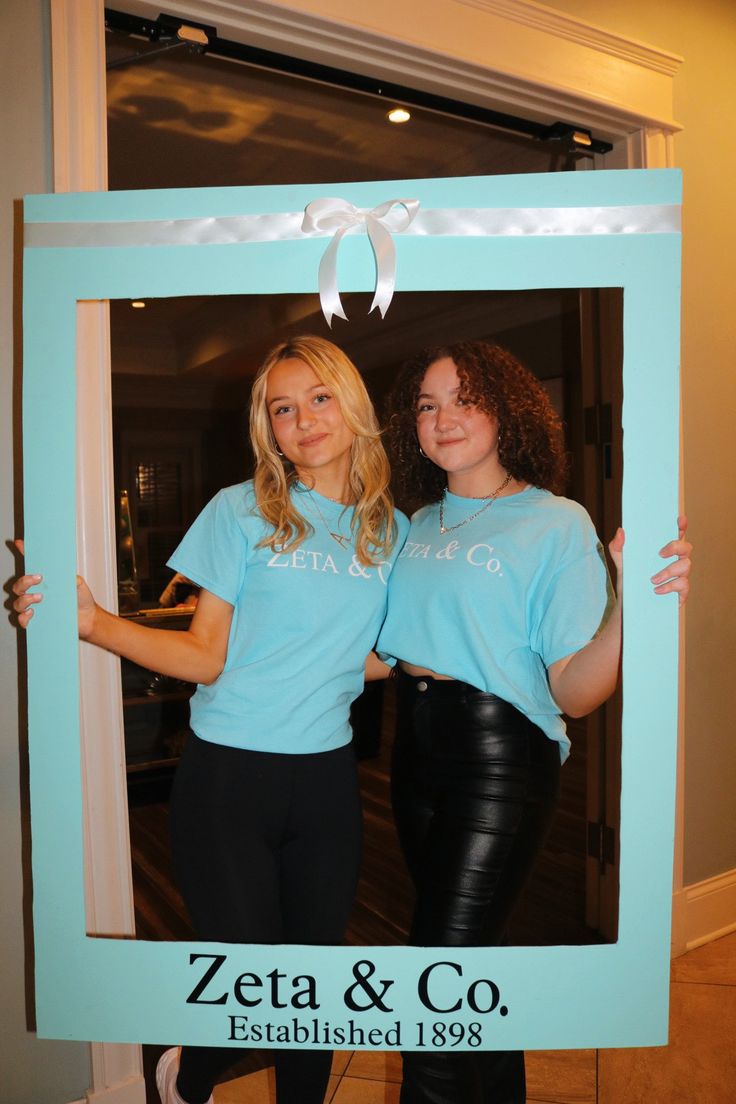 two women standing in front of a photo frame with the word zeta & co on it