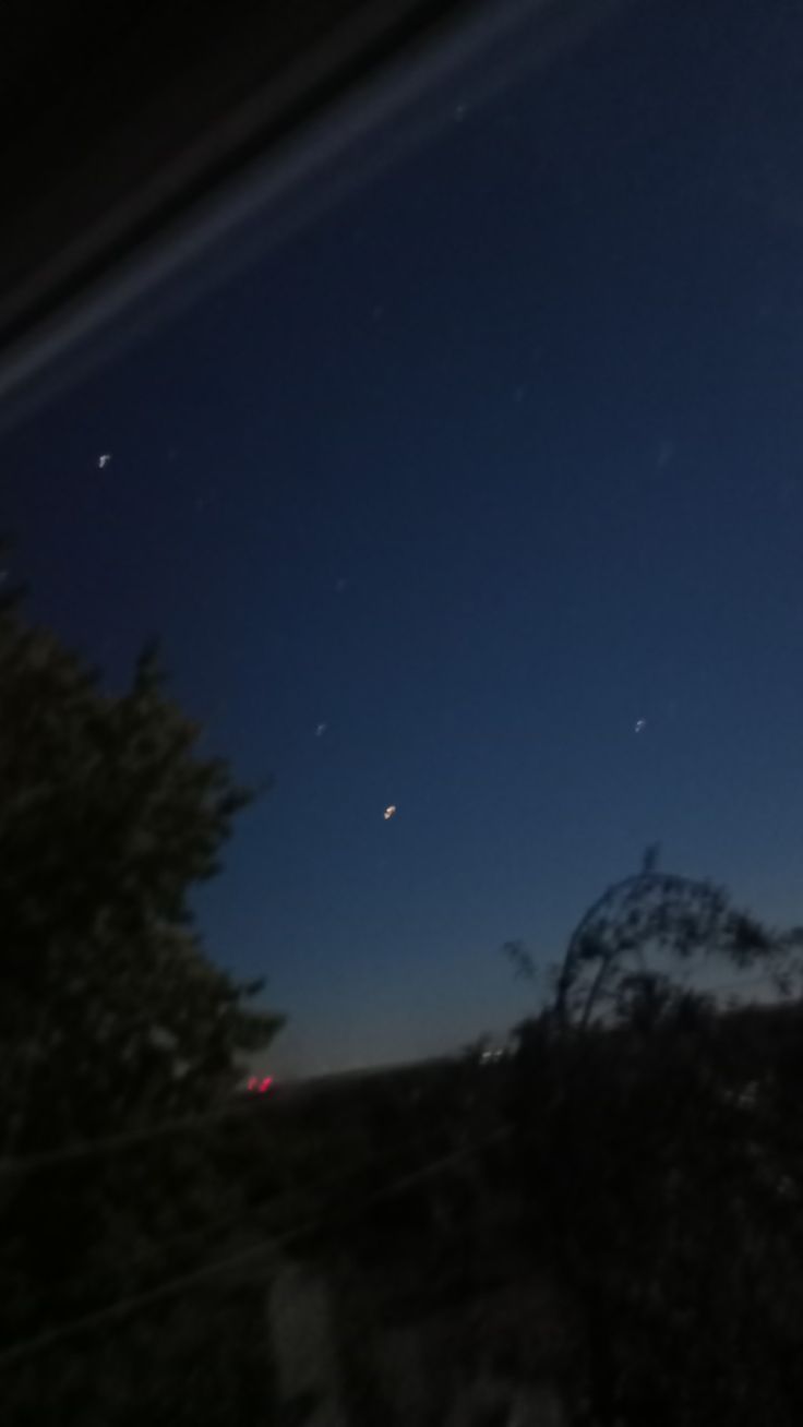 the night sky is lit up with stars and moon in the distance, as seen from an outside window