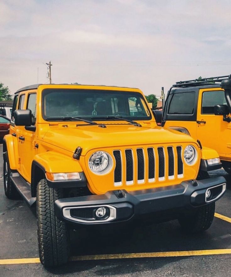 two bright yellow jeeps are parked in a parking lot with other vehicles behind them