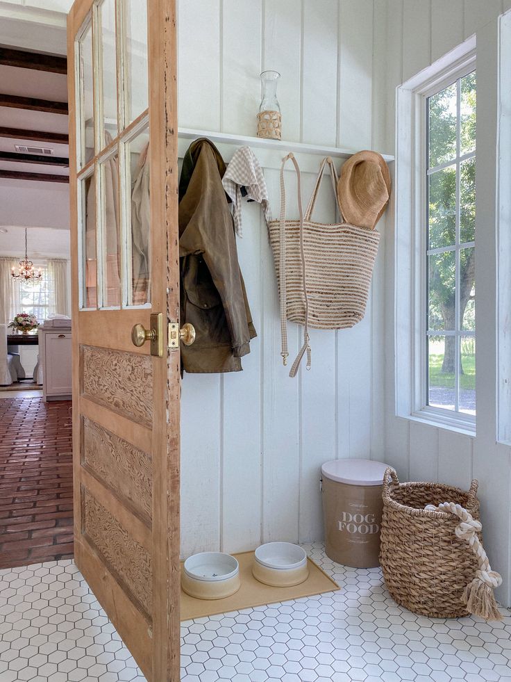 the inside of a house with white walls and wooden doors, baskets on hooks, and clothes hanging from the wall