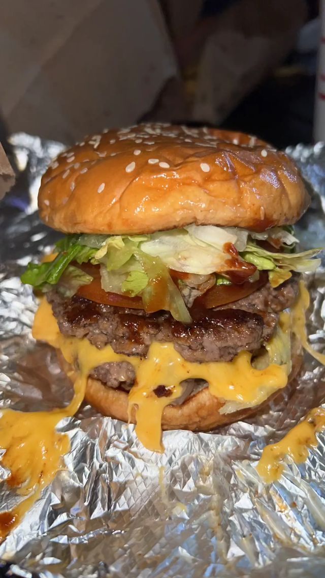 a cheeseburger with lettuce and tomato on it sitting on tin foil