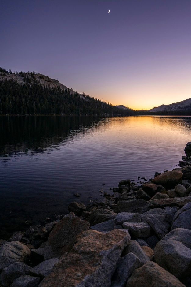 the sun is setting over a lake with rocks and trees on it, as well as mountains in the distance