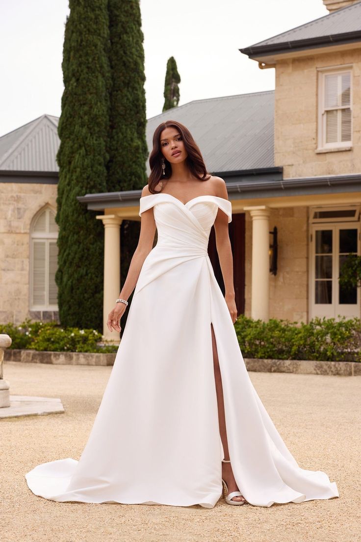 a woman standing in front of a house wearing a white wedding dress with thigh high slit