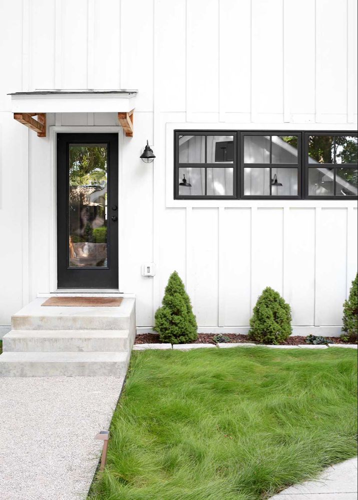 a white house with black doors and steps leading up to the front door is surrounded by green grass