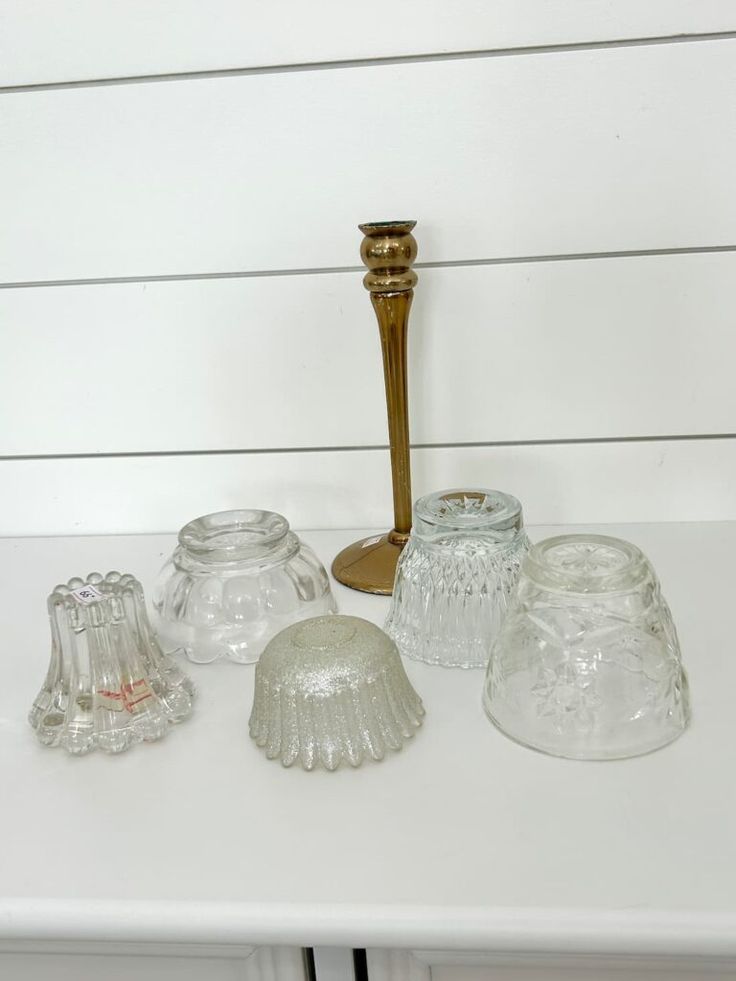 an assortment of glass items on a white table with a gold candle holder in the background