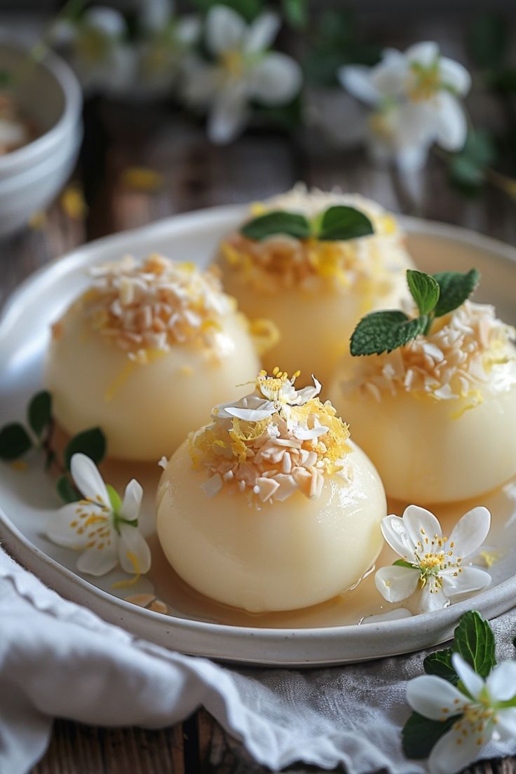 Four delicate desserts topped with shredded coconut, lemon zest, and mint leaves, garnished with white blossoms. Lemon Holiday Desserts, Christmas Flavors Desserts, Light Lemon Desserts, Winter Dessert Ideas, Tea Time Recipes, Entremet Recipe, Lemon Diy, Tea Desserts, Lemon Tart Recipe